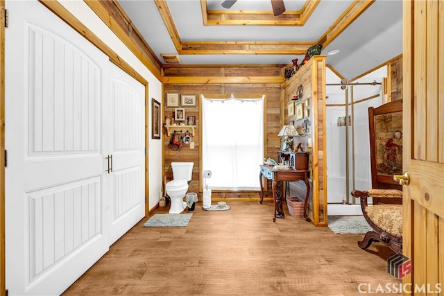 living area featuring ceiling fan, a tray ceiling, wood walls, and wood finished floors