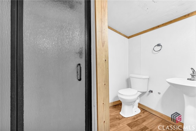 bathroom featuring toilet, a sink, wood finished floors, baseboards, and crown molding