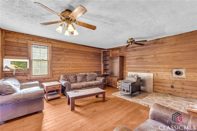 living area featuring a wood stove, light wood-style floors, ceiling fan, and a textured ceiling