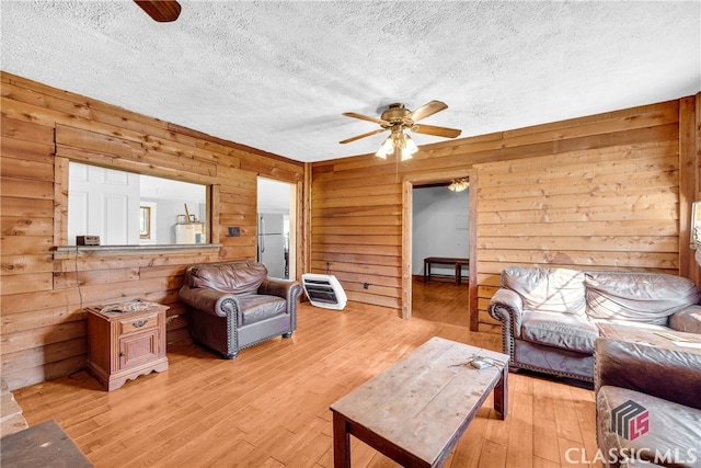 living area featuring ceiling fan, a textured ceiling, light wood-style flooring, and wooden walls