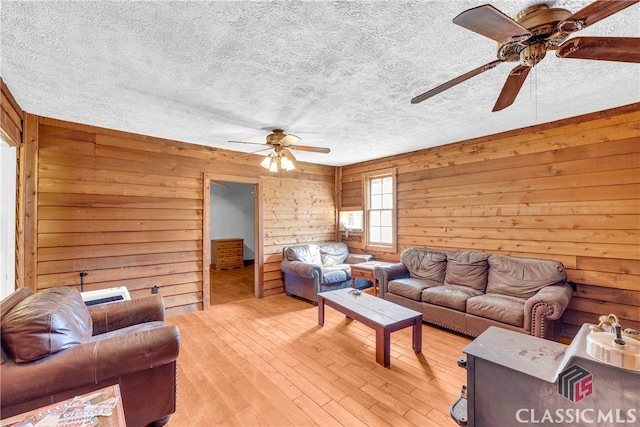 living area with a textured ceiling, wood walls, light wood-type flooring, and a ceiling fan