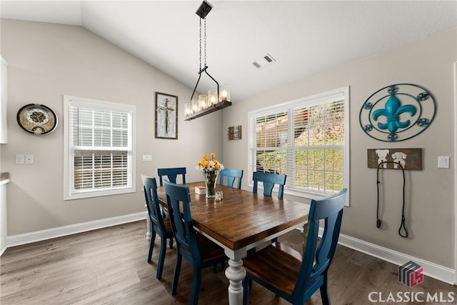 dining area with lofted ceiling, a notable chandelier, visible vents, baseboards, and dark wood-style floors