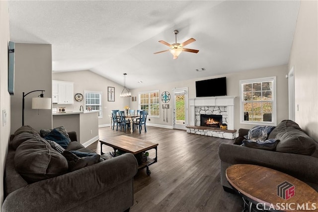 living room with lofted ceiling, dark wood-style flooring, a healthy amount of sunlight, and a stone fireplace