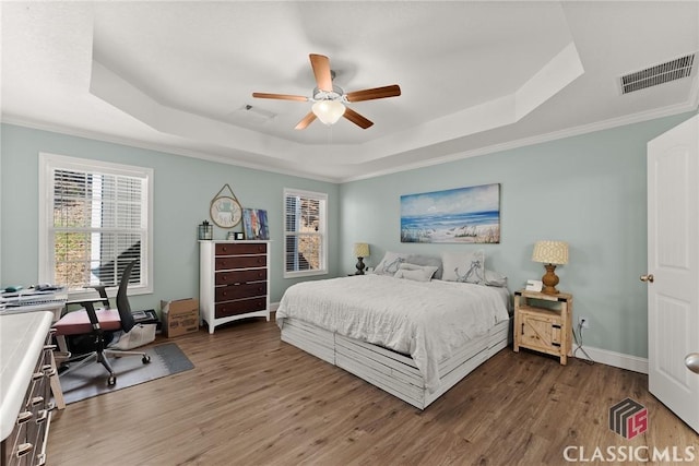 bedroom featuring baseboards, visible vents, a tray ceiling, and wood finished floors