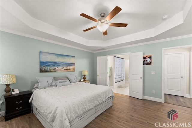 bedroom featuring baseboards, a raised ceiling, ceiling fan, wood finished floors, and crown molding