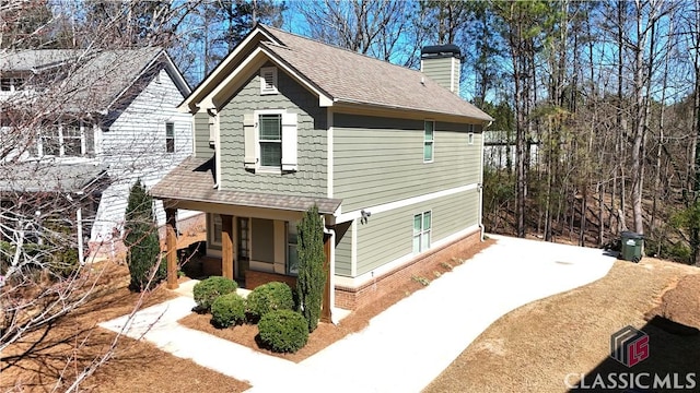 view of home's exterior with covered porch, roof with shingles, brick siding, and a chimney