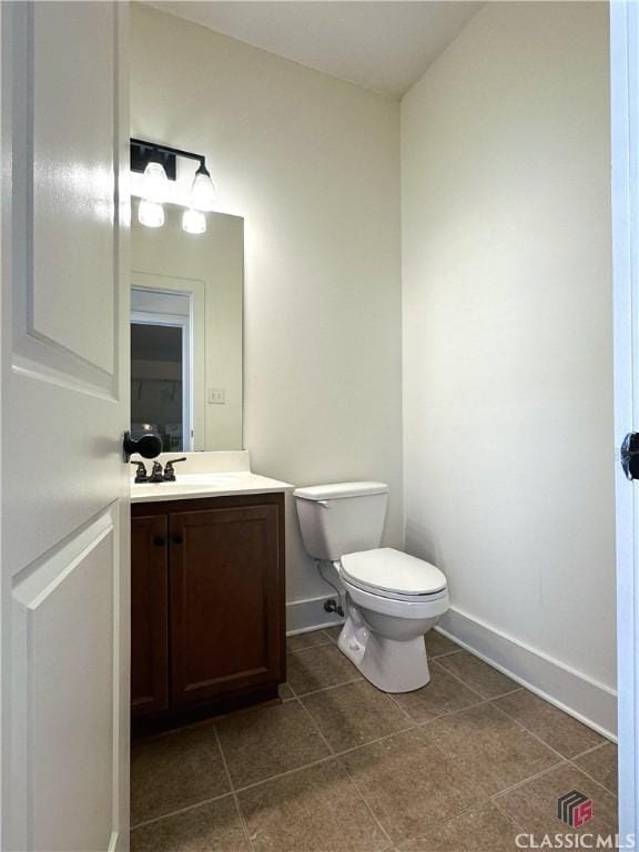 half bathroom featuring toilet, tile patterned flooring, vanity, and baseboards