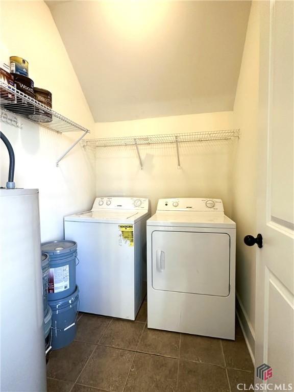 clothes washing area with water heater, laundry area, dark tile patterned floors, and washer and dryer