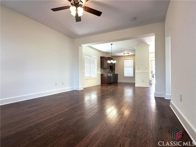 unfurnished living room with ceiling fan with notable chandelier, dark wood-style flooring, a sink, and baseboards