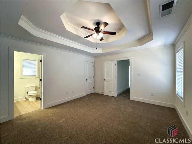 unfurnished bedroom featuring carpet flooring, visible vents, ornamental molding, a raised ceiling, and ensuite bath