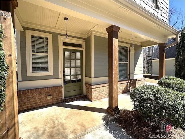 view of exterior entry featuring a porch and brick siding