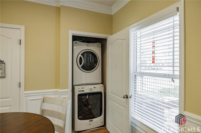 washroom featuring stacked washing maching and dryer, laundry area, crown molding, and a wainscoted wall