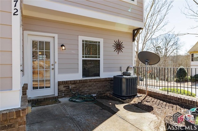 view of exterior entry featuring a patio, brick siding, fence, and central air condition unit