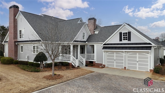 view of front facade featuring concrete driveway, a standing seam roof, a chimney, and roof with shingles