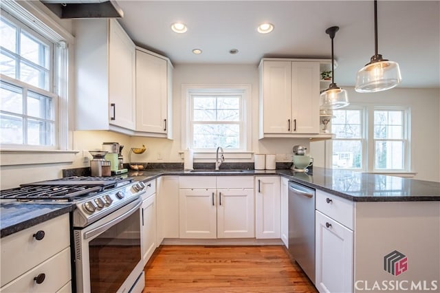 kitchen with white cabinets, dark stone countertops, a peninsula, stainless steel appliances, and a sink