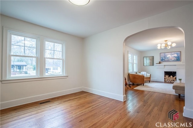 interior space with arched walkways, a fireplace, wood finished floors, visible vents, and baseboards