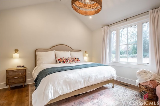 bedroom with baseboards, visible vents, vaulted ceiling, and wood finished floors