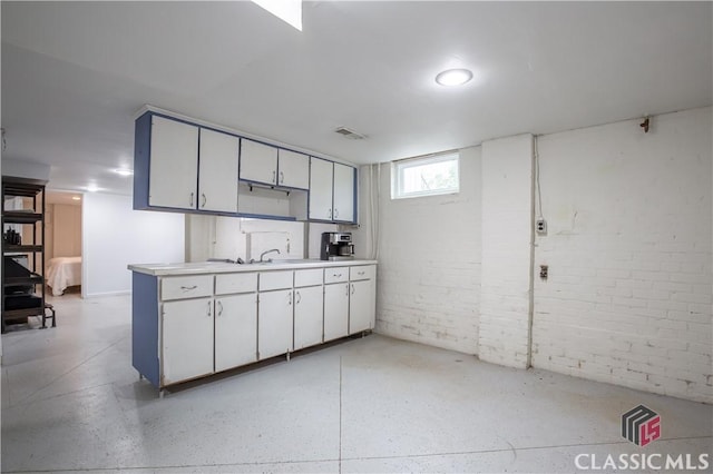 kitchen with brick wall, a sink, visible vents, white cabinetry, and light countertops