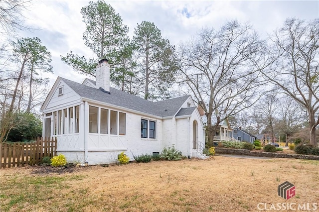 view of side of home featuring brick siding, fence, a sunroom, crawl space, and a chimney