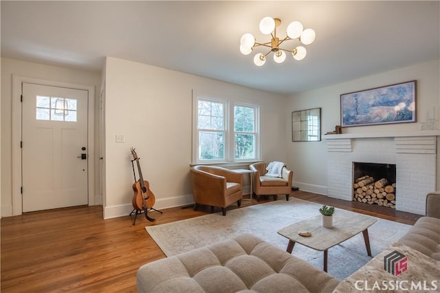 living area featuring a notable chandelier, a fireplace, wood finished floors, and baseboards