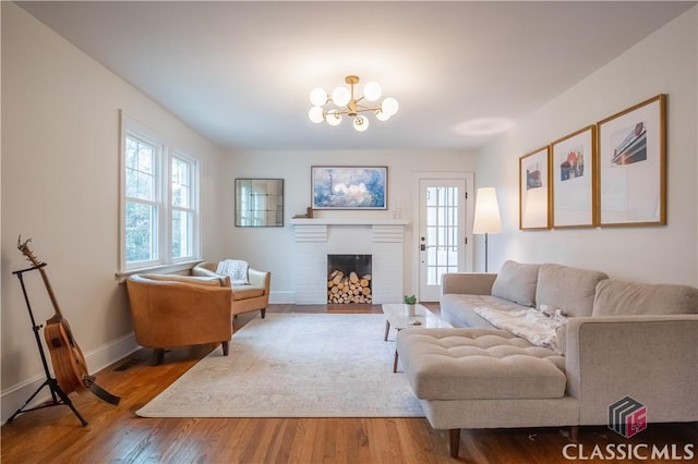 living area featuring a chandelier, a brick fireplace, baseboards, and wood finished floors