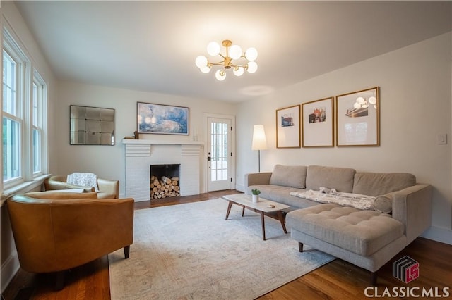 living area with a brick fireplace, plenty of natural light, an inviting chandelier, and wood finished floors