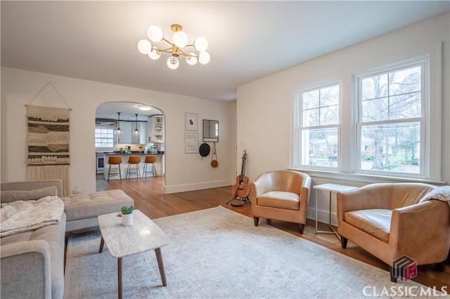 living area featuring arched walkways, baseboards, wood finished floors, and a notable chandelier