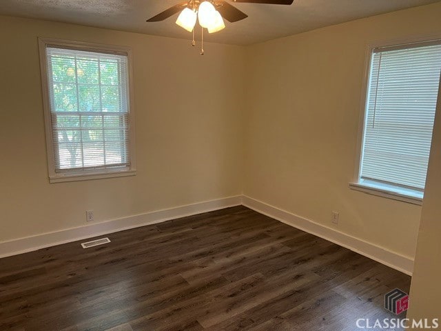 empty room with dark wood-style floors, visible vents, baseboards, and a ceiling fan