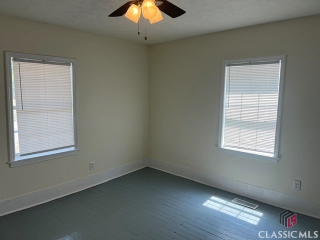 empty room with visible vents, dark wood-style flooring, a ceiling fan, and baseboards