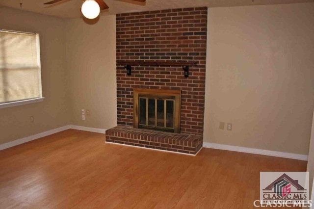 unfurnished living room with a fireplace, wood finished floors, a ceiling fan, and baseboards