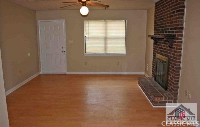 unfurnished living room featuring a brick fireplace, baseboards, and wood finished floors