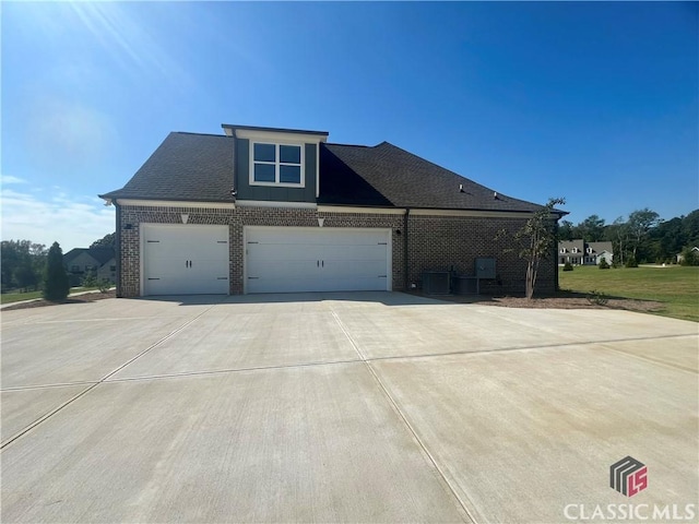 view of front of house featuring a garage, concrete driveway, brick siding, and roof with shingles