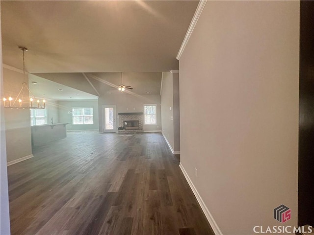 unfurnished living room with baseboards, a glass covered fireplace, dark wood-type flooring, crown molding, and ceiling fan with notable chandelier