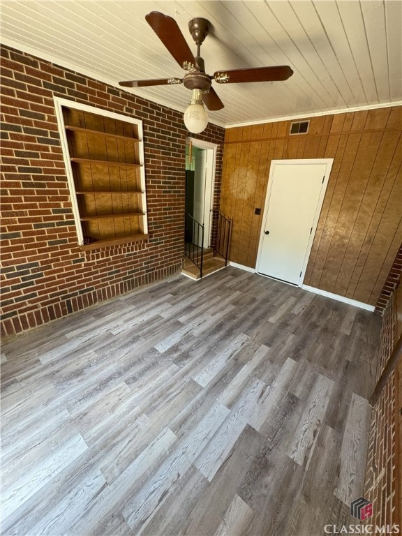 interior space with ceiling fan, brick wall, wood finished floors, visible vents, and wood ceiling