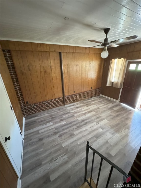 unfurnished room with ceiling fan, wood walls, and light wood-type flooring