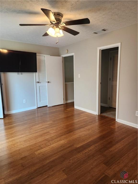 unfurnished living room featuring visible vents, a textured ceiling, baseboards, and wood finished floors