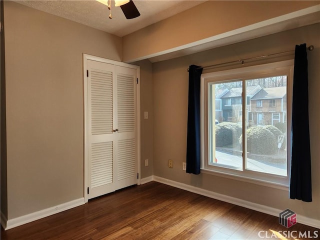 unfurnished bedroom with dark wood-type flooring, a ceiling fan, baseboards, and a closet