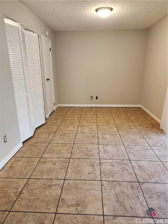 empty room featuring light tile patterned floors, baseboards, and a textured ceiling