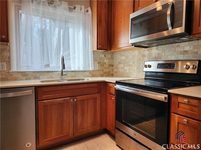 kitchen with backsplash, light countertops, brown cabinets, stainless steel appliances, and a sink