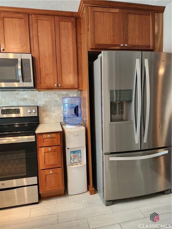 kitchen with brown cabinetry, appliances with stainless steel finishes, tasteful backsplash, and light countertops