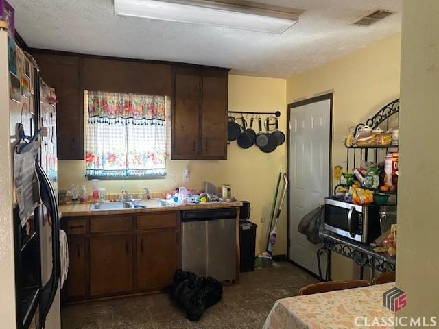 kitchen with dark brown cabinetry, stainless steel appliances, a sink, visible vents, and light countertops