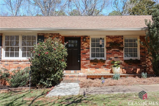 property entrance featuring covered porch, brick siding, and a shingled roof