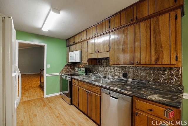 kitchen with dark countertops, backsplash, light wood-style flooring, appliances with stainless steel finishes, and a sink