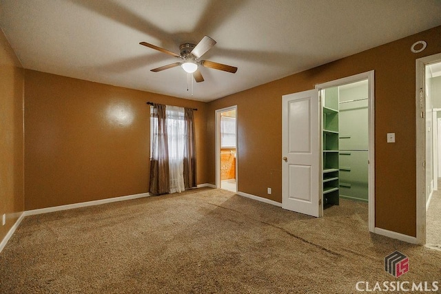 unfurnished bedroom with carpet, ceiling fan, a spacious closet, and baseboards