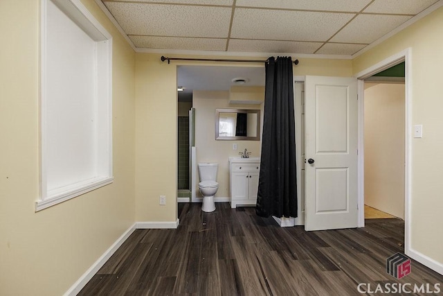 corridor featuring dark wood-style flooring, a drop ceiling, a sink, and baseboards