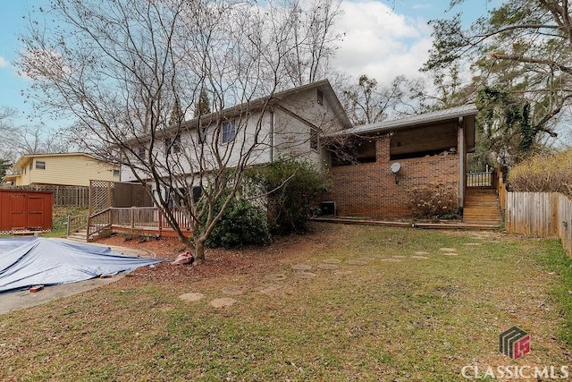 back of property with an outbuilding, brick siding, a yard, fence, and a deck