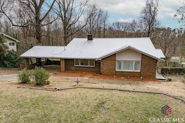 single story home with metal roof, brick siding, driveway, a carport, and a chimney