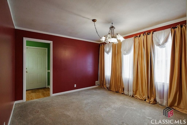 carpeted spare room featuring crown molding, baseboards, and an inviting chandelier