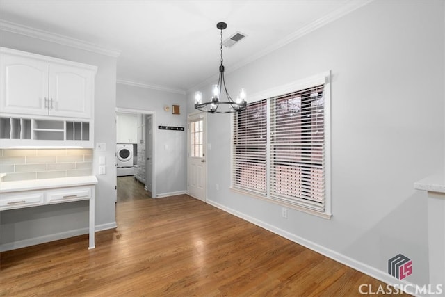 unfurnished dining area with a notable chandelier, baseboards, ornamental molding, light wood-type flooring, and washer / dryer