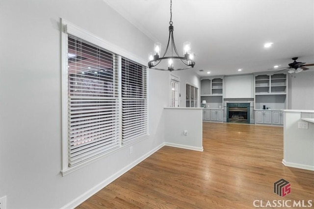 unfurnished dining area featuring ceiling fan, recessed lighting, a fireplace, baseboards, and light wood-style floors